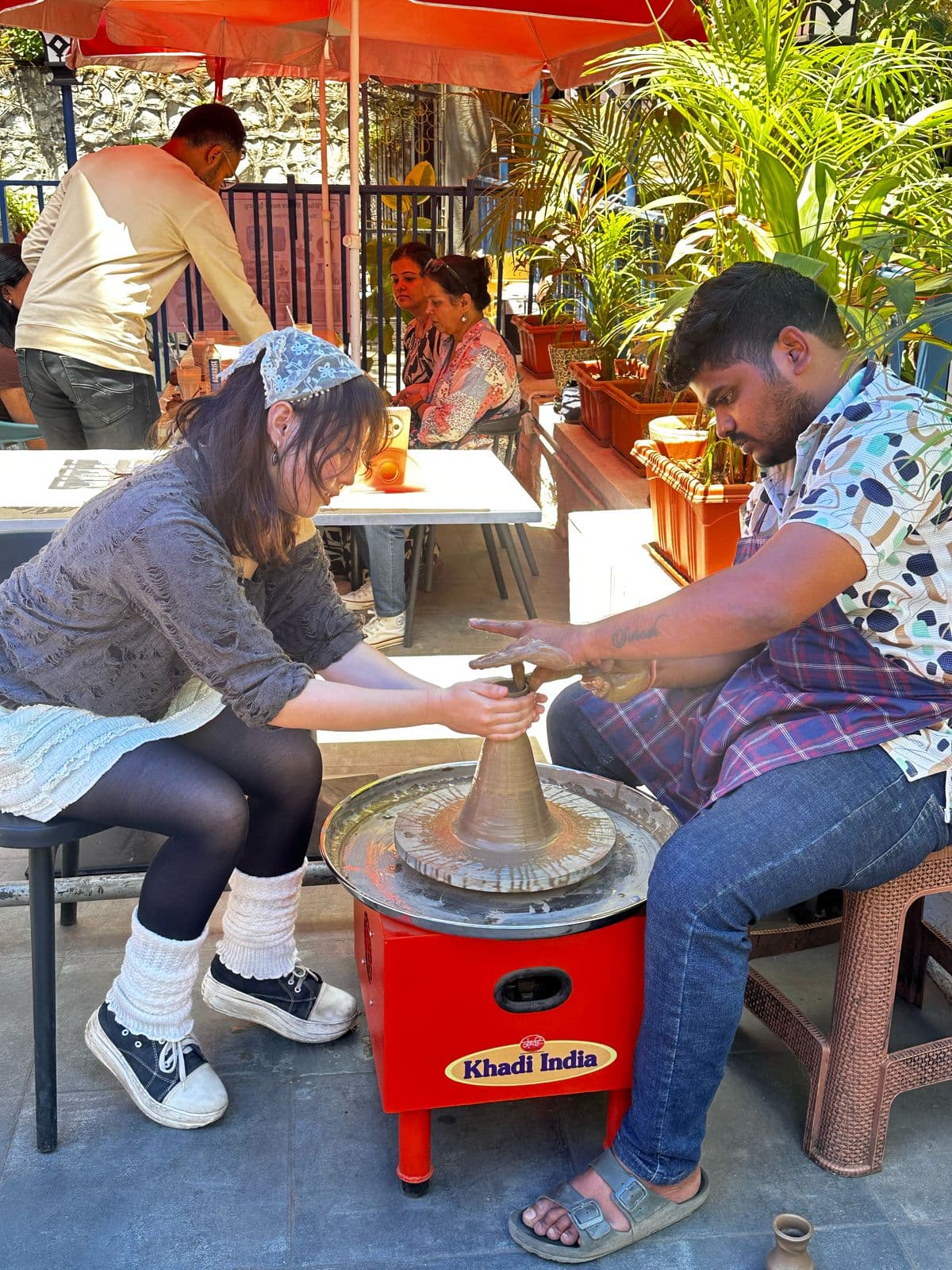 Instructor guiding a beginner at a pottery wheel