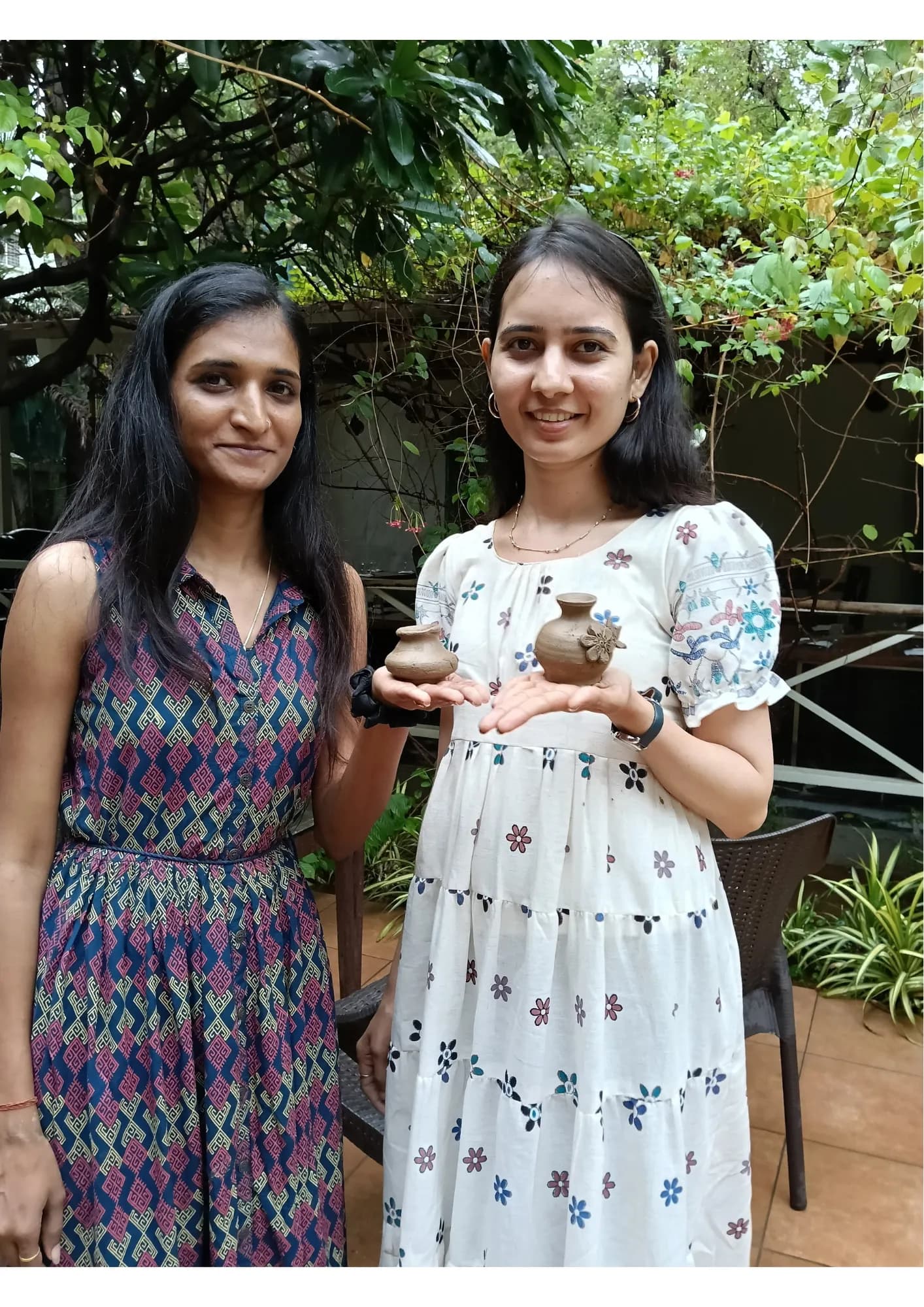 Two women smiling and holding up small handmade clay pots.