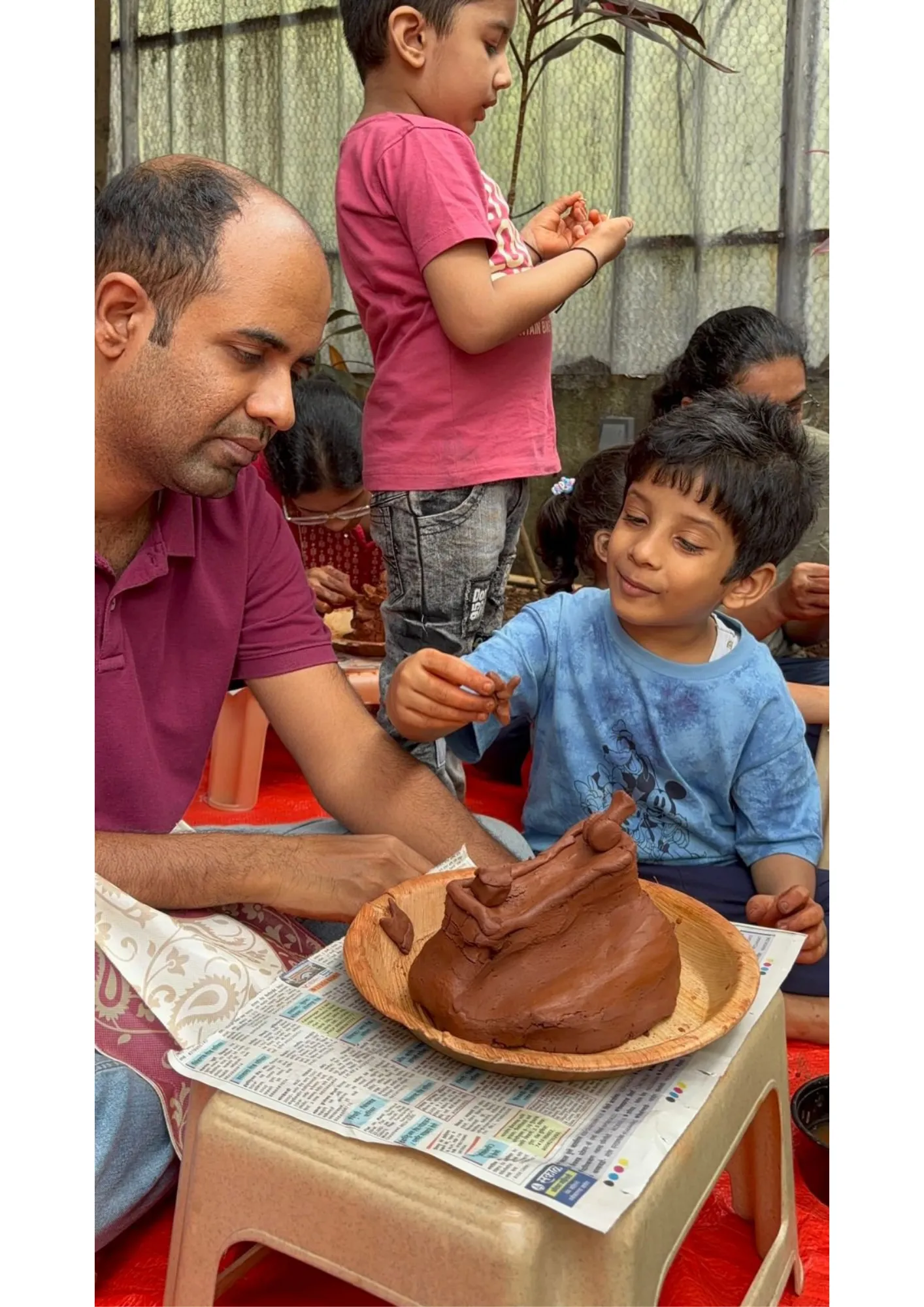 A large group of people smiling and holding clay Ganesha outdoors.