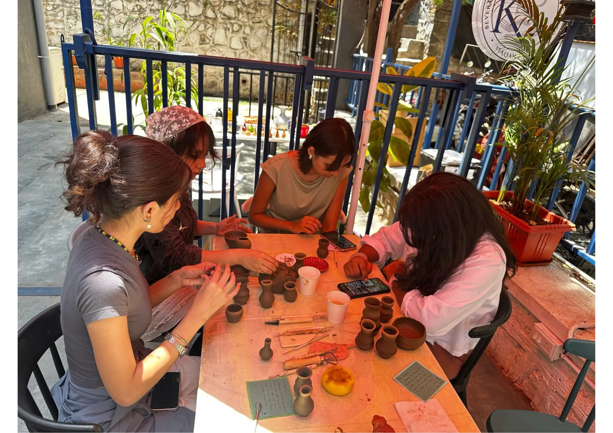 Four women sitting around an outdoor table working with clay.